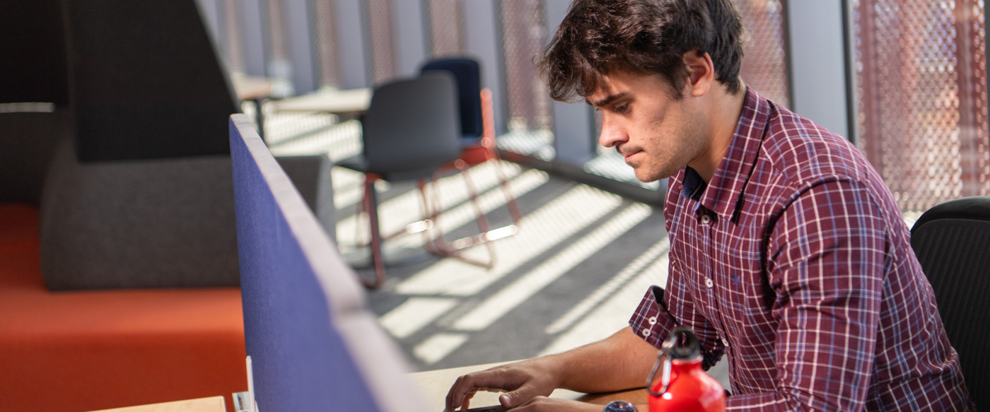 Male student looking at laptop screen in James McCune Smith Learning Hub with red water bottle in foreground