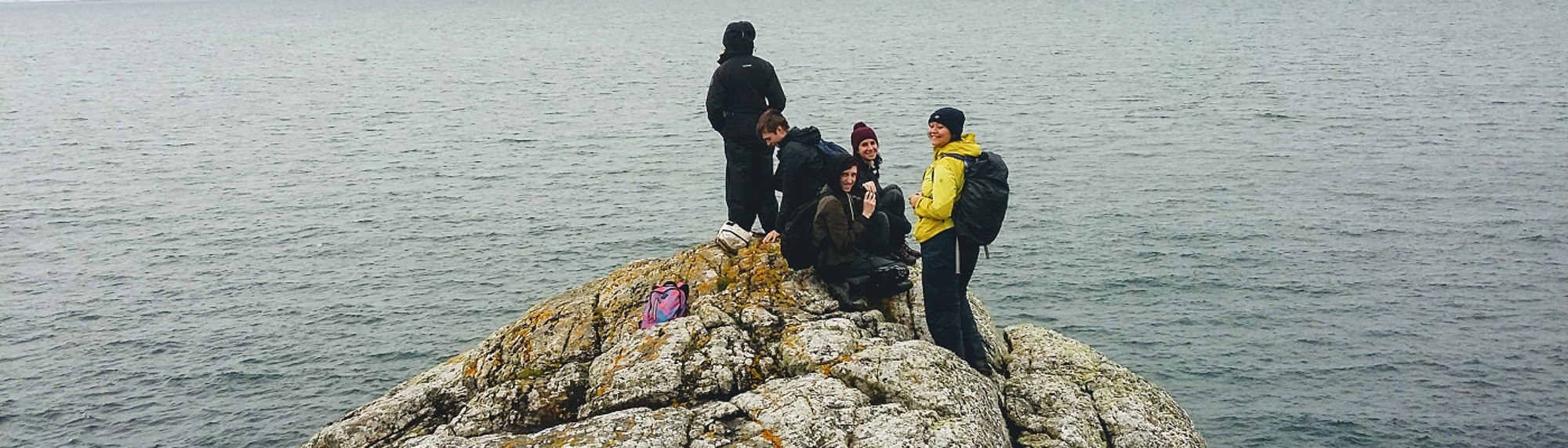 Students on the rocks by the sea - 1400x400