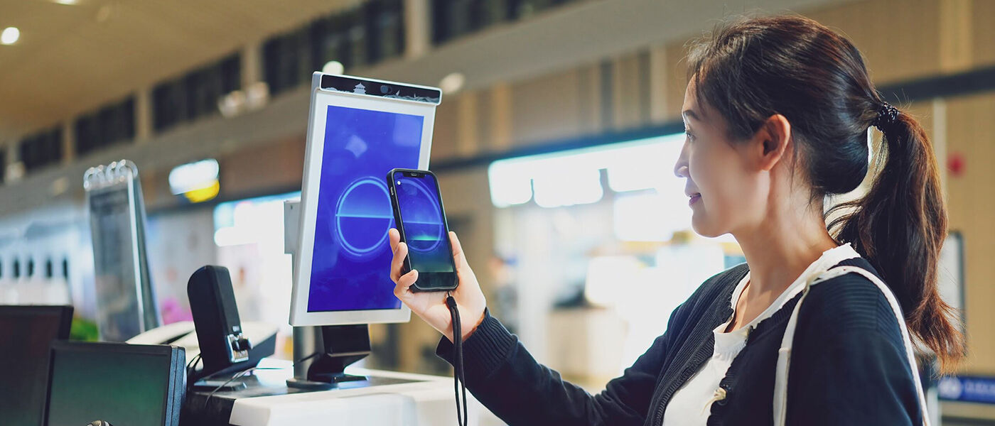 A woman looks at a mobile phone screen. The phone screen is mirrored on a larger tablet screen behind the phone.