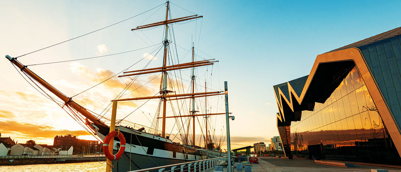 Photograph of the river Clyde, showing Glasgow's Riverside Museum and the Glenlee Tall Ship, illuminated by a warm light near sunset.