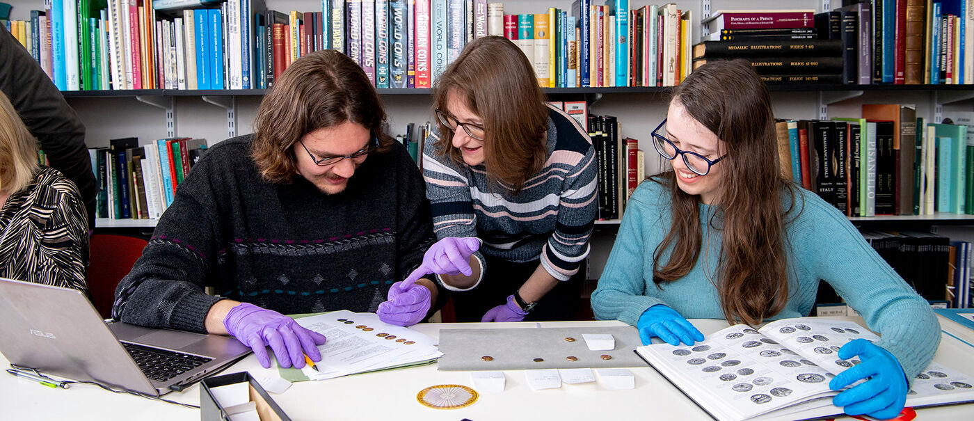 Students examining ancient coins with the help of a tutor