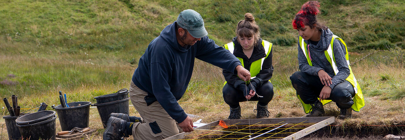 A tutor showing students on archaeological fieldwork how to use a planning frame. 