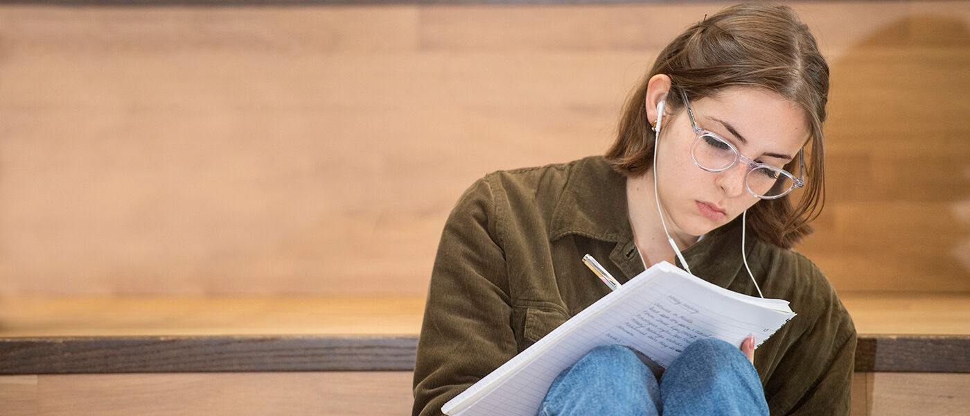 A student sits on stairs writing in a notebook