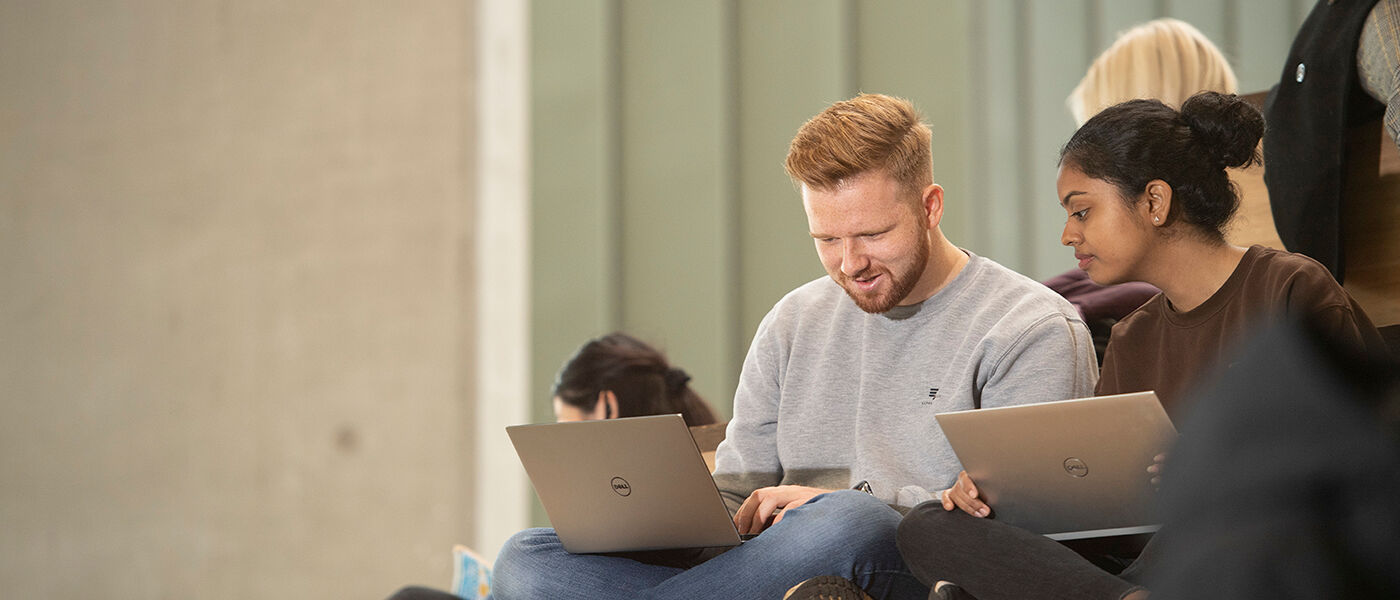 Two students with laptops having a conversation