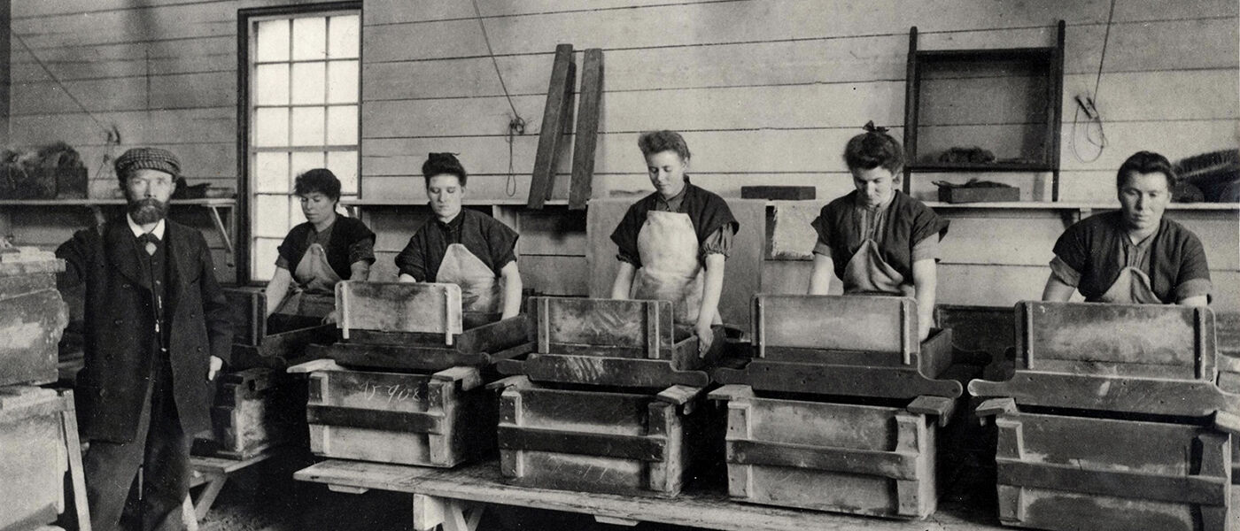 Late 19th century photo of a man overseeing a line of women working in a factory.