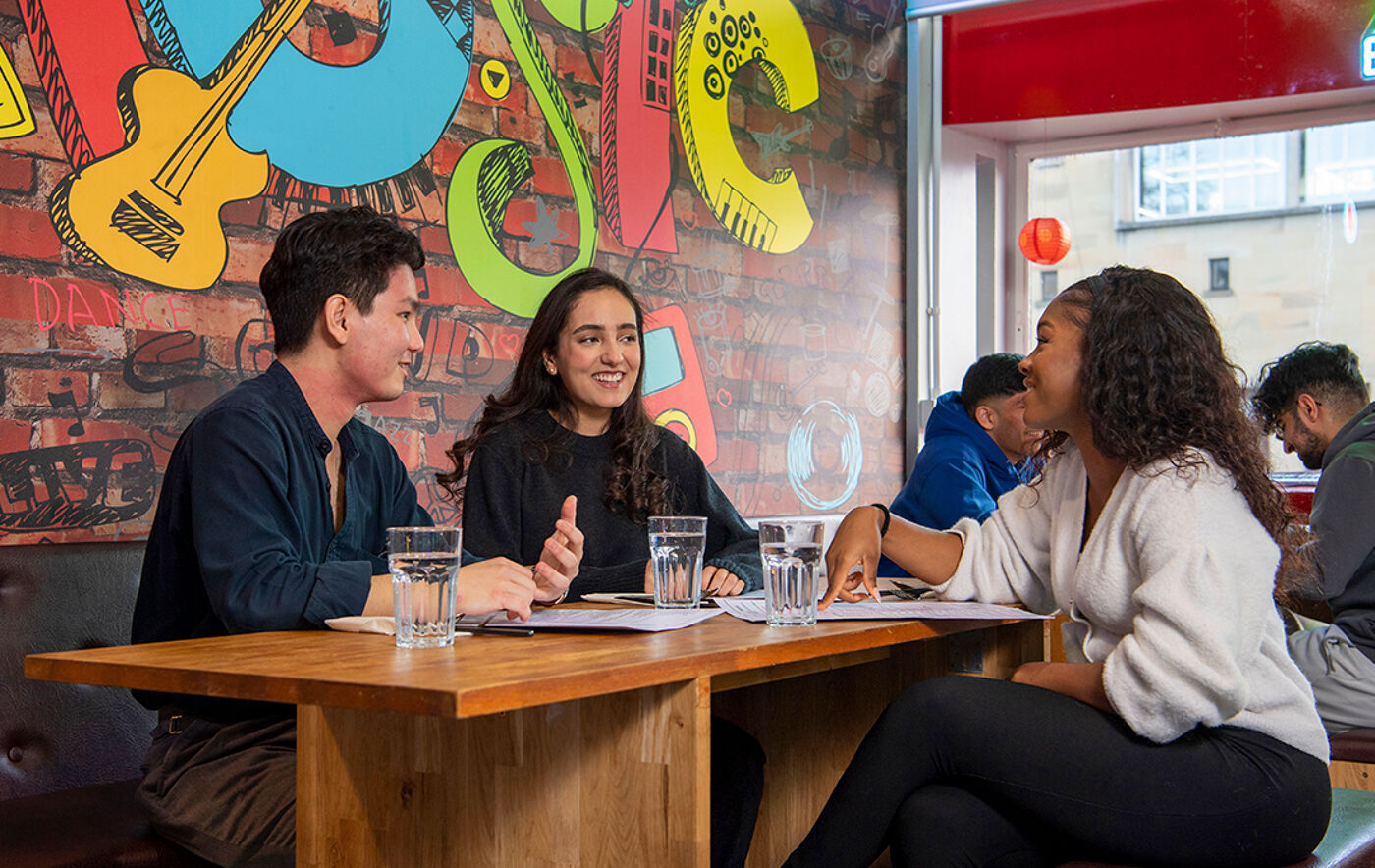 three students sitting chatting and smiling under a brightly coloured wall