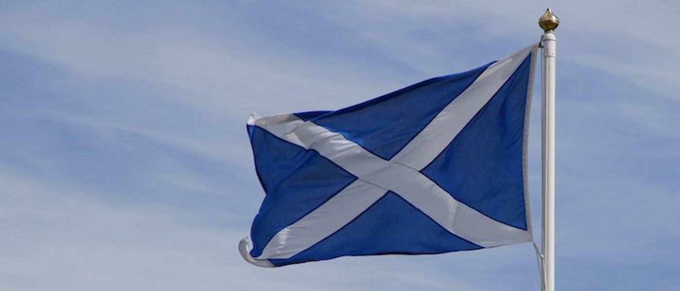 A Saltire flag - a diagonal white cross on a dark blue backgound -  flying against a light blue sky