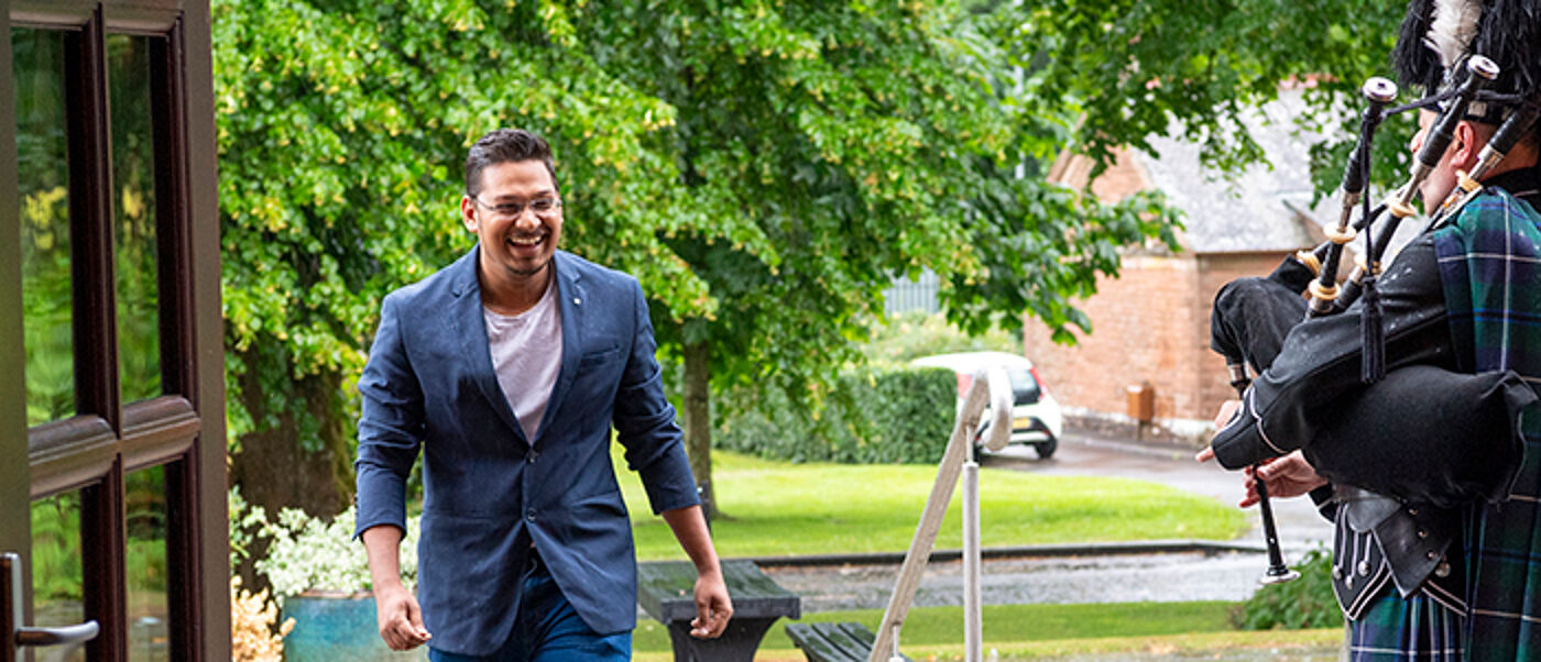A student walking up stairs to enter a building with someone playing the bag pipes at the door