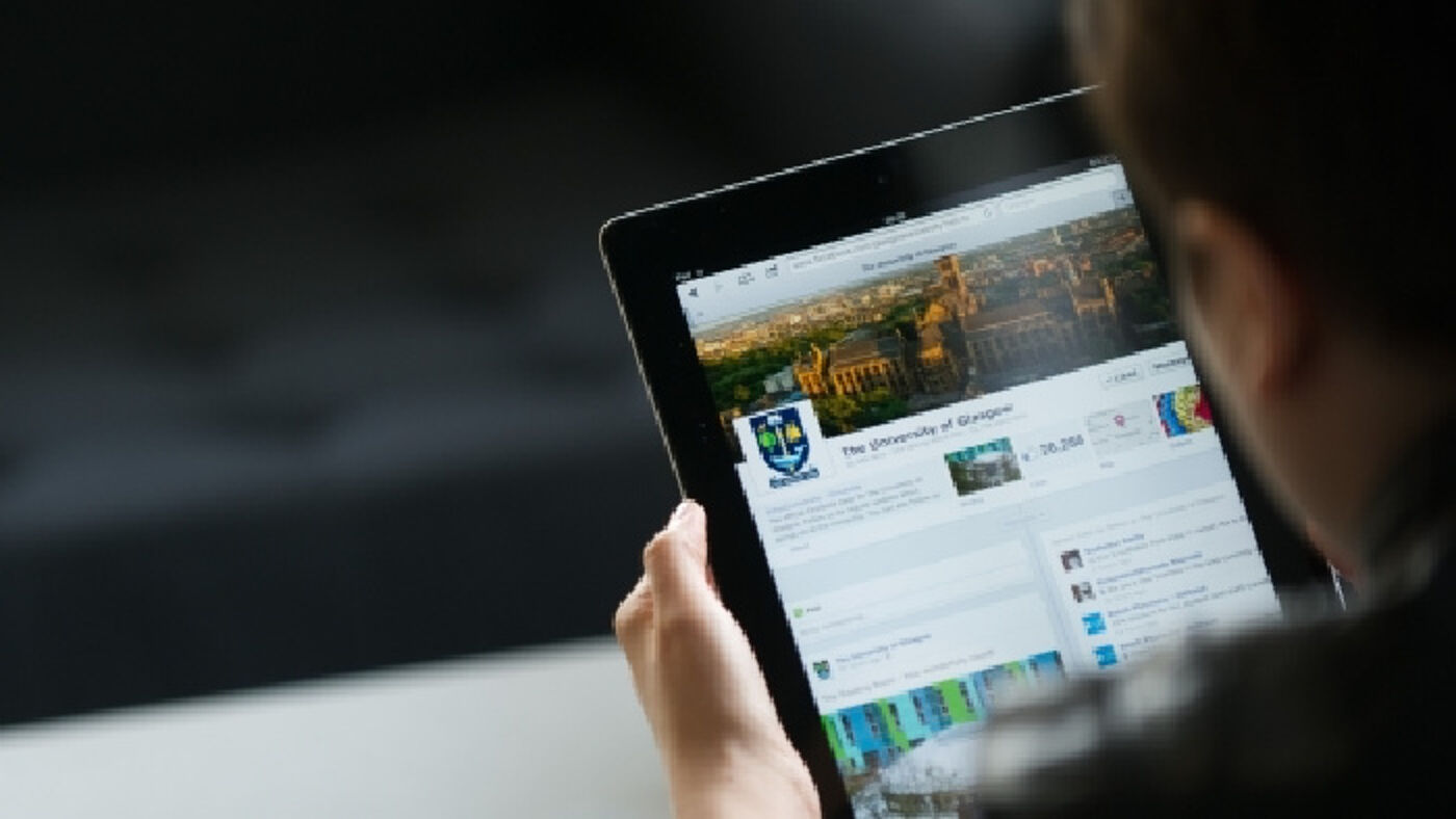 Hand holding a tablet with the screen showing the University of Glasgow LinkedIn homepage