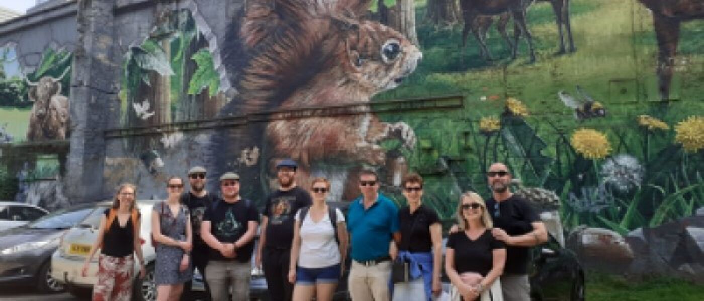 Group of people smiling for a photo underneath Glasgow Street Art of a Squirrel