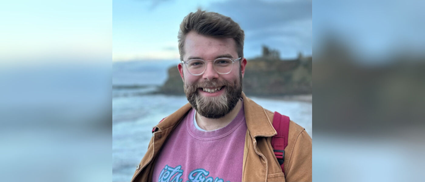 Man with beard smiling with the sea behind him
