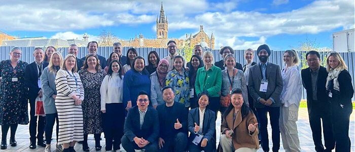 Attendees of the Stakeholder Summit posing in a group outside in the sunshine, with the Gilbert Scott Building tower in the background