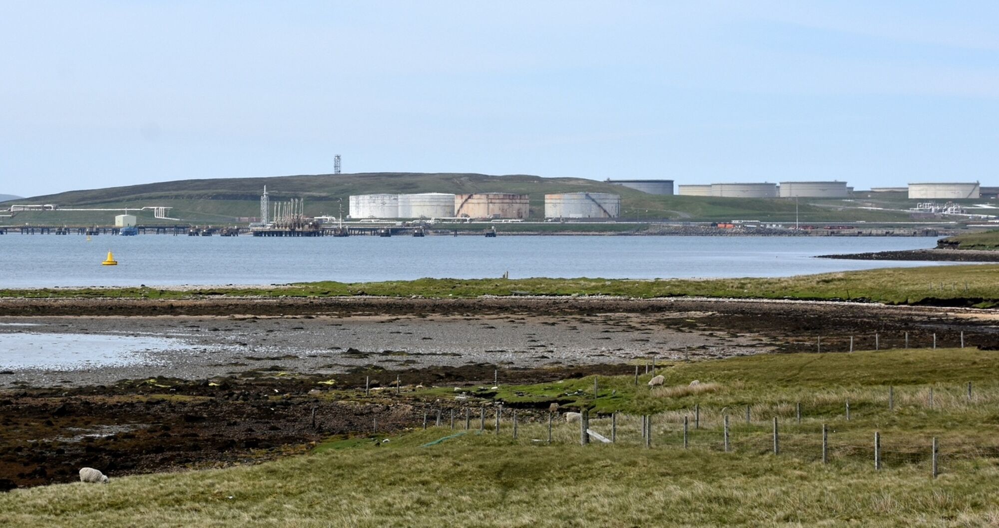 A view of Sullom Voe oil terminal with industrial building on the shore of an inlet of the sea. Photo credit: James Stringer, Flickr https://www.flickr.com/photos/jamesstringer/48068245541/