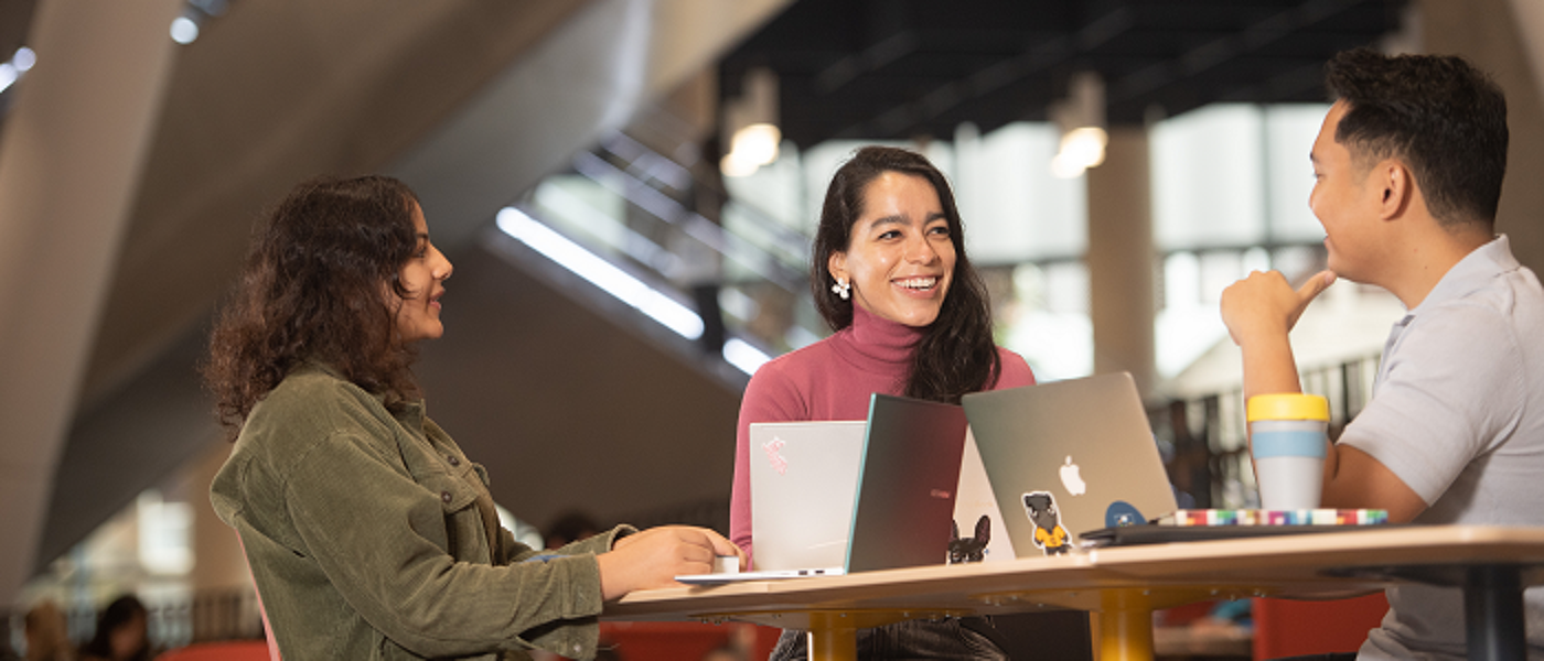 Three students sitting at a table with laptops