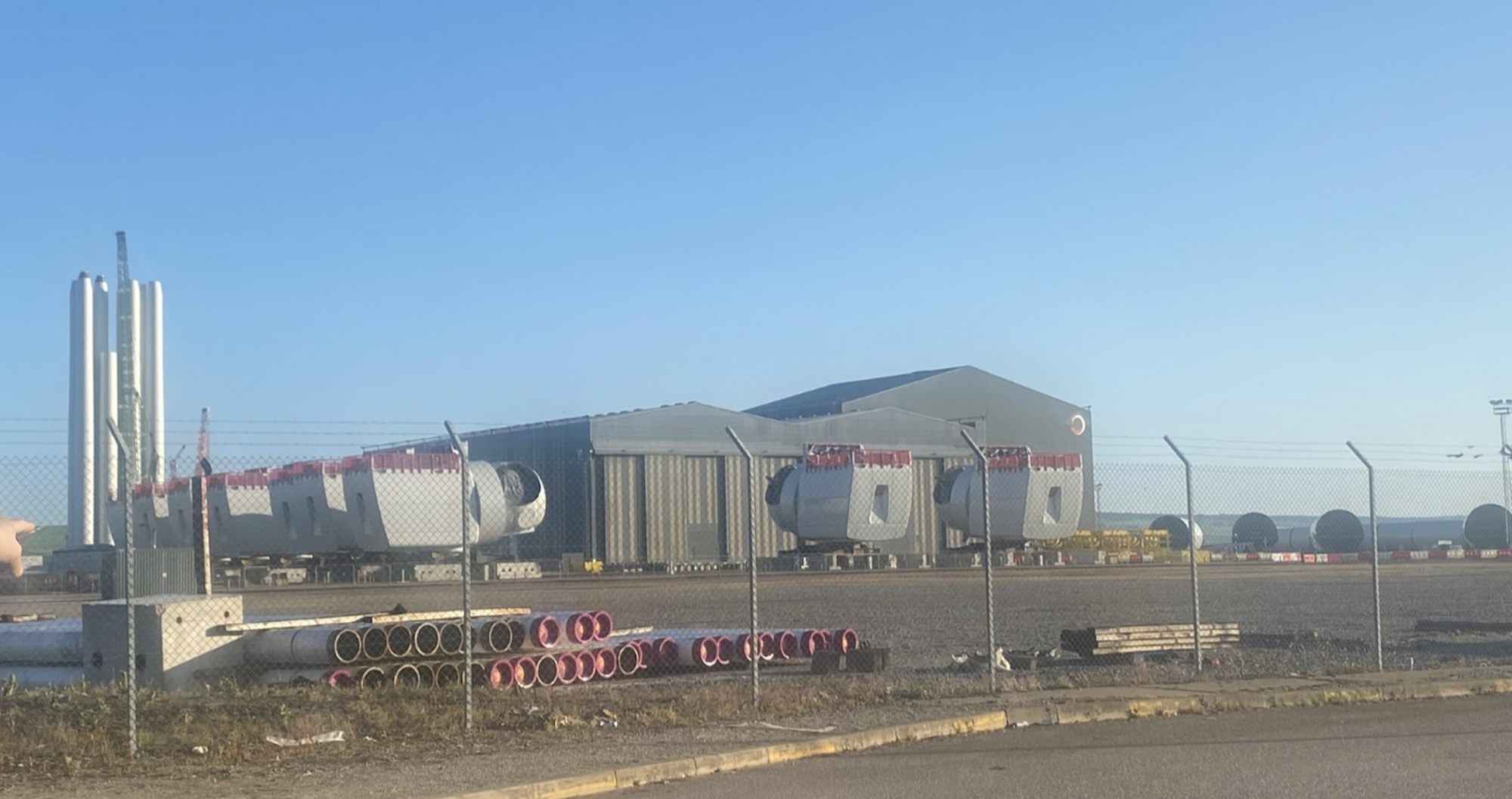 View of a construction yard with a shed and large pieces of equipment against a blue sky. Photo credit: Ewan Gibbs