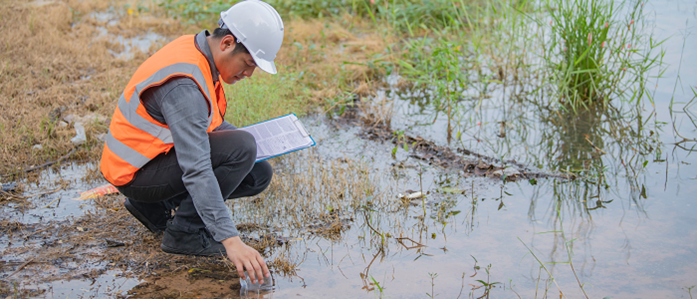 Man in hard hat and high viz vest taking a water sample from field