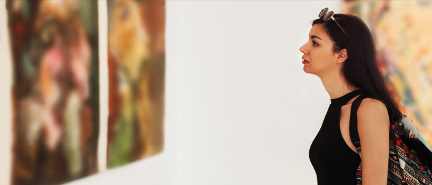 Photograph of a student in a gallery studying a painting.