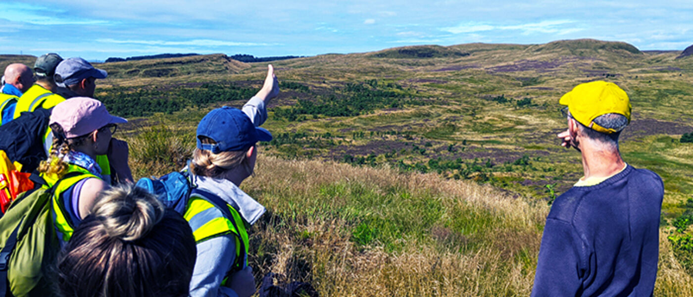Photograph of students planning an archaeological dig looking out over heather covered hills.