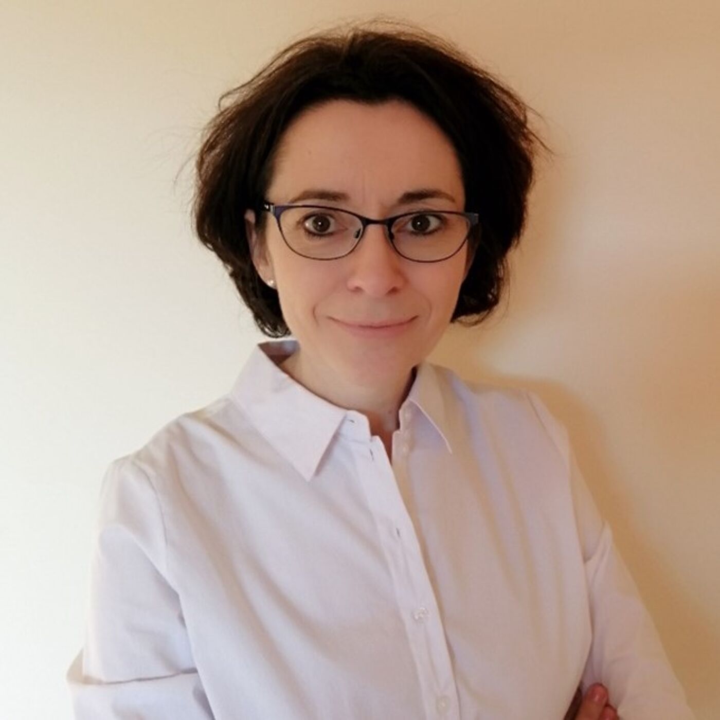 Person wearing a crisp white button-up shirt with arms crossed, standing against a plain beige background.
