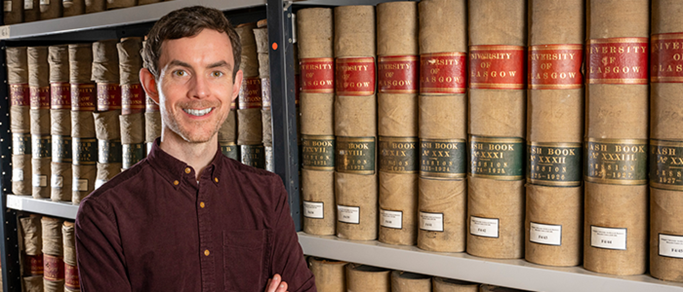 Michael Gallagher, Archivist, posing with Archives books on shelves
