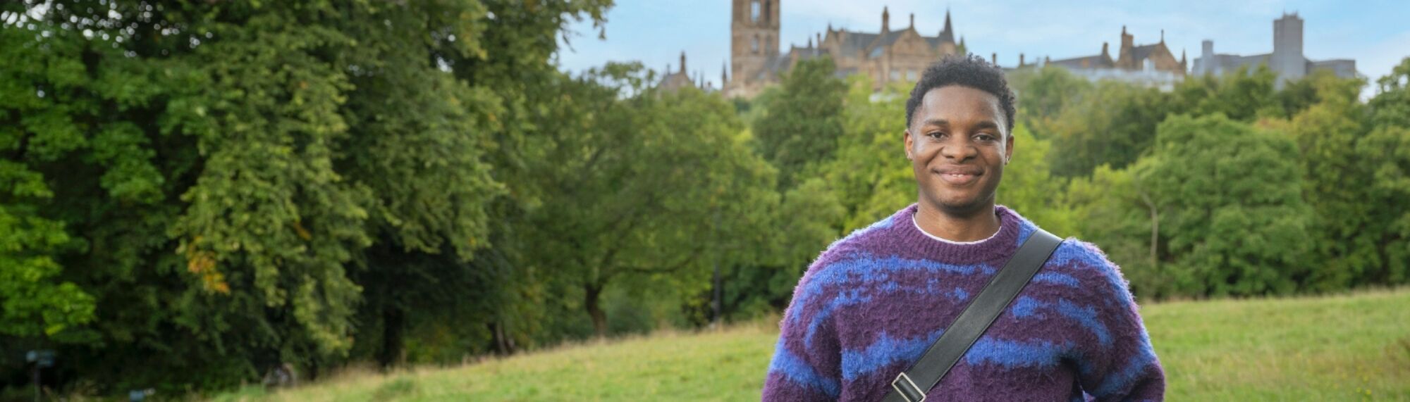 A student in Kelvingrove Park with the University of Glasgow tower in the distance