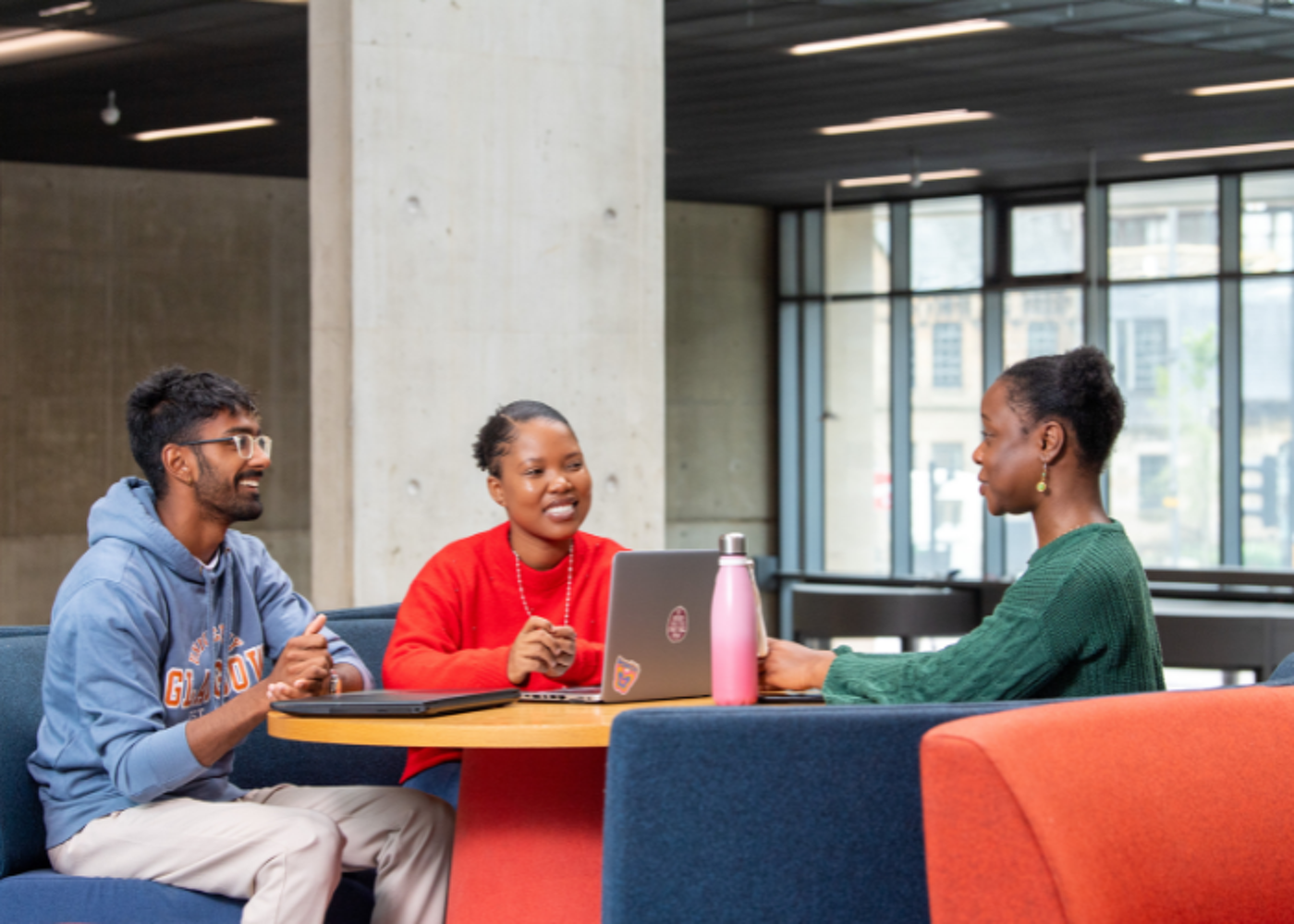 Students sitting around a table with laptops talking and smiling