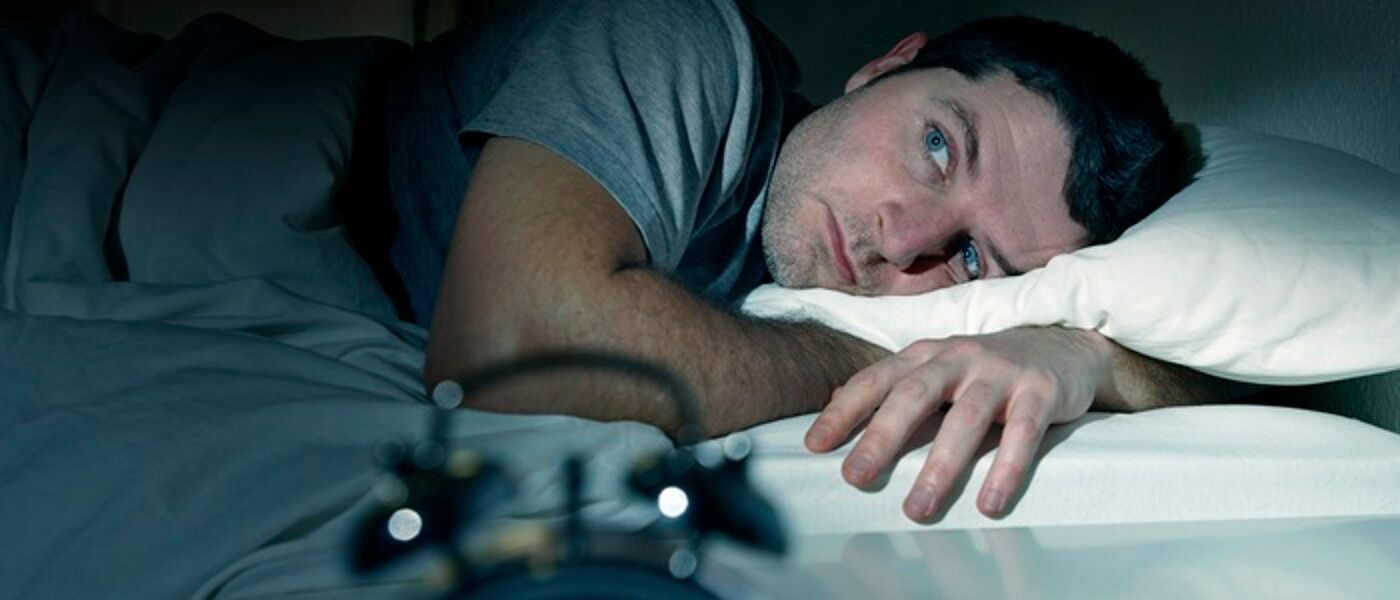 Man lying awake in bed with an alarm clock in the foreground