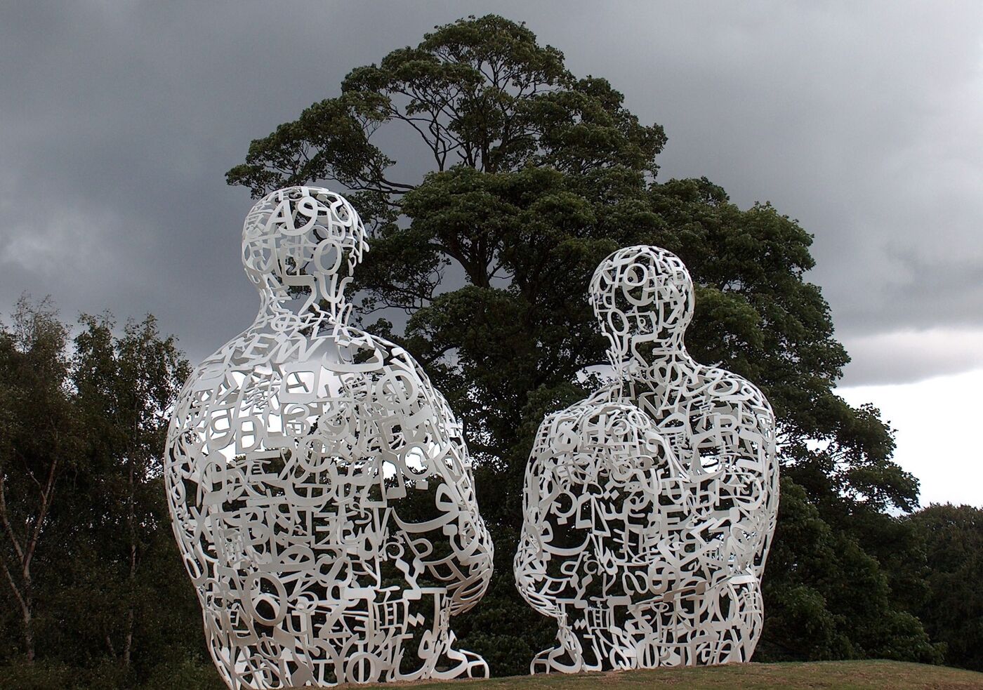 Two sculpted human figures made of letters sitting under a tree