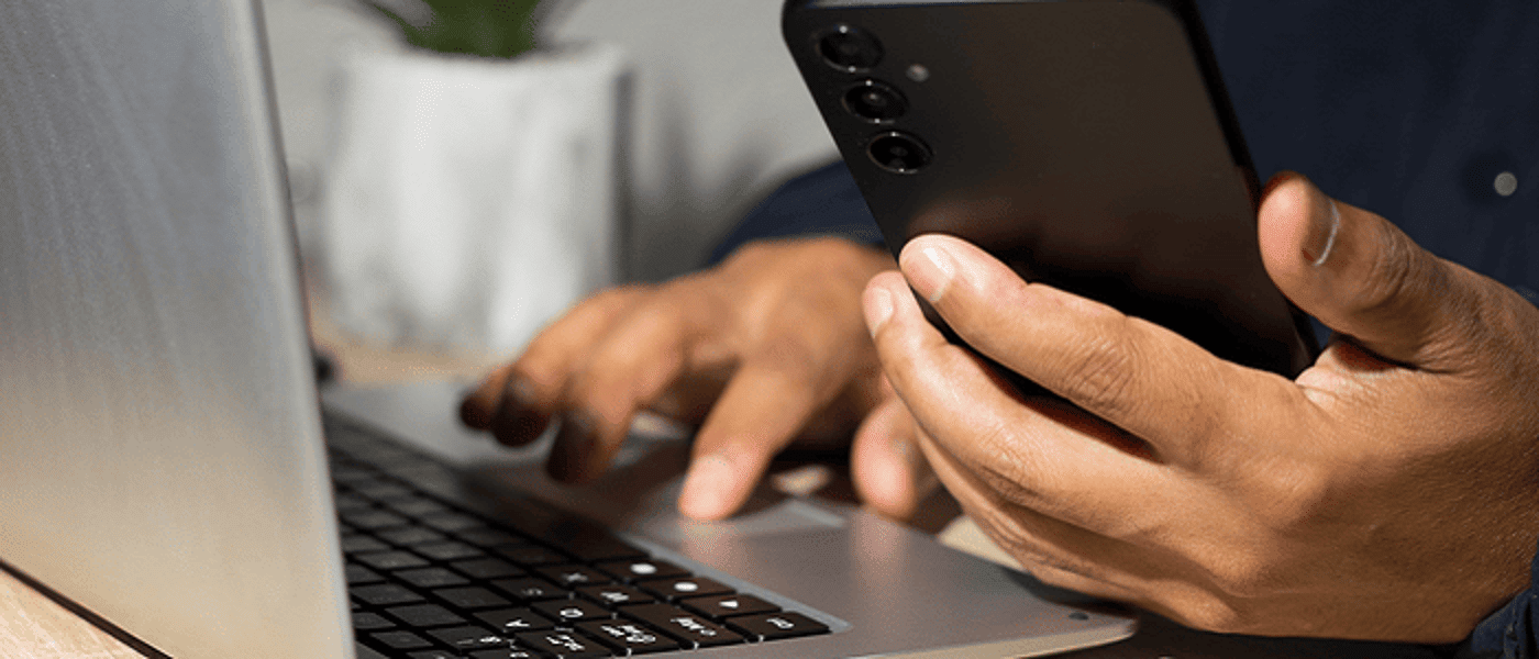 Close up of hand holding a mobile phone with laptop in front