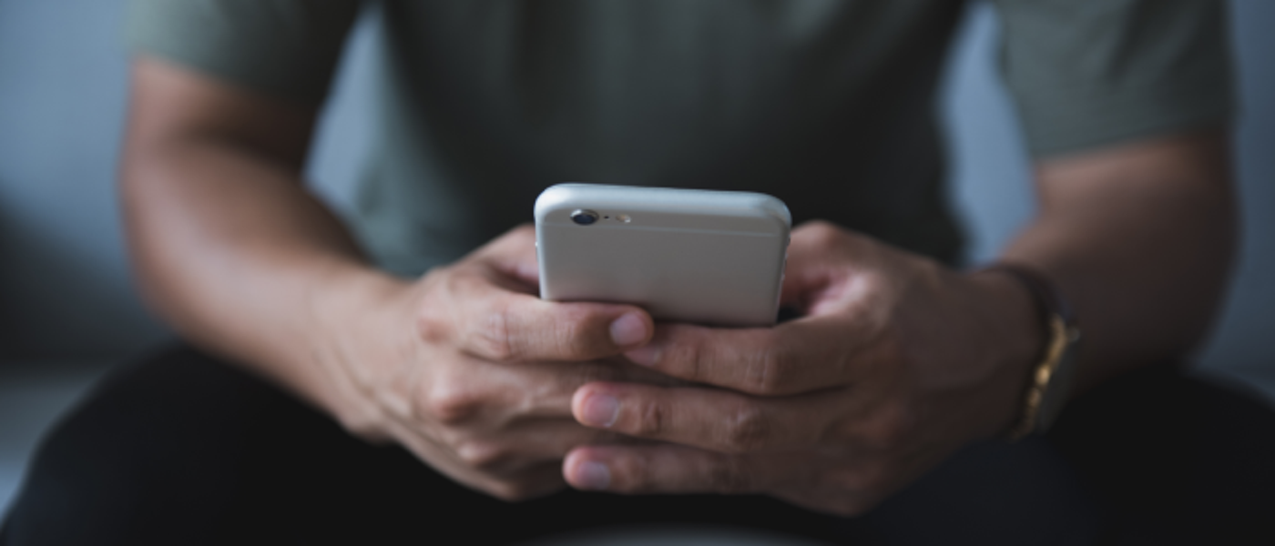 Young man hand holding cell phone on the sofa in the living room. He was reading and answering emails and shopping online on weekends at home.