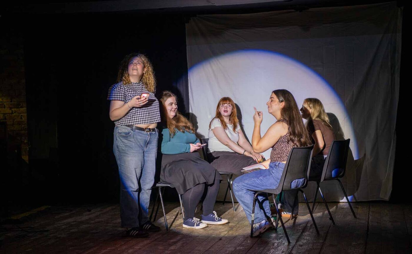 a group of people, 4 sitting and one standing in a spotlight