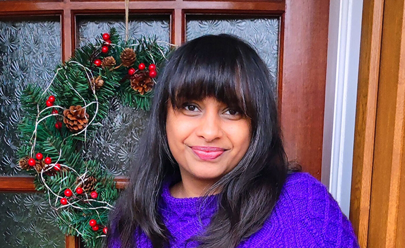 Lovleen Kushwah standing at a door with a Christmas wreath hanging in the background