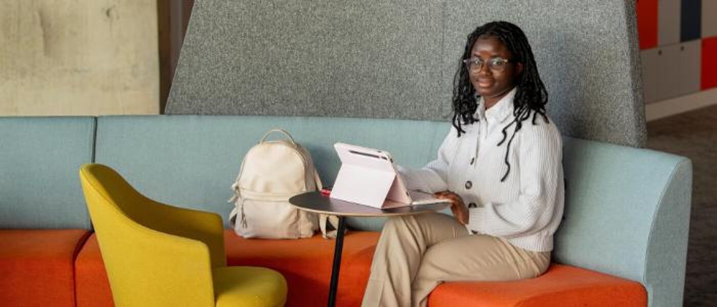 Student sitting with laptop in James McCune Smith Learning Hub and looking to camera