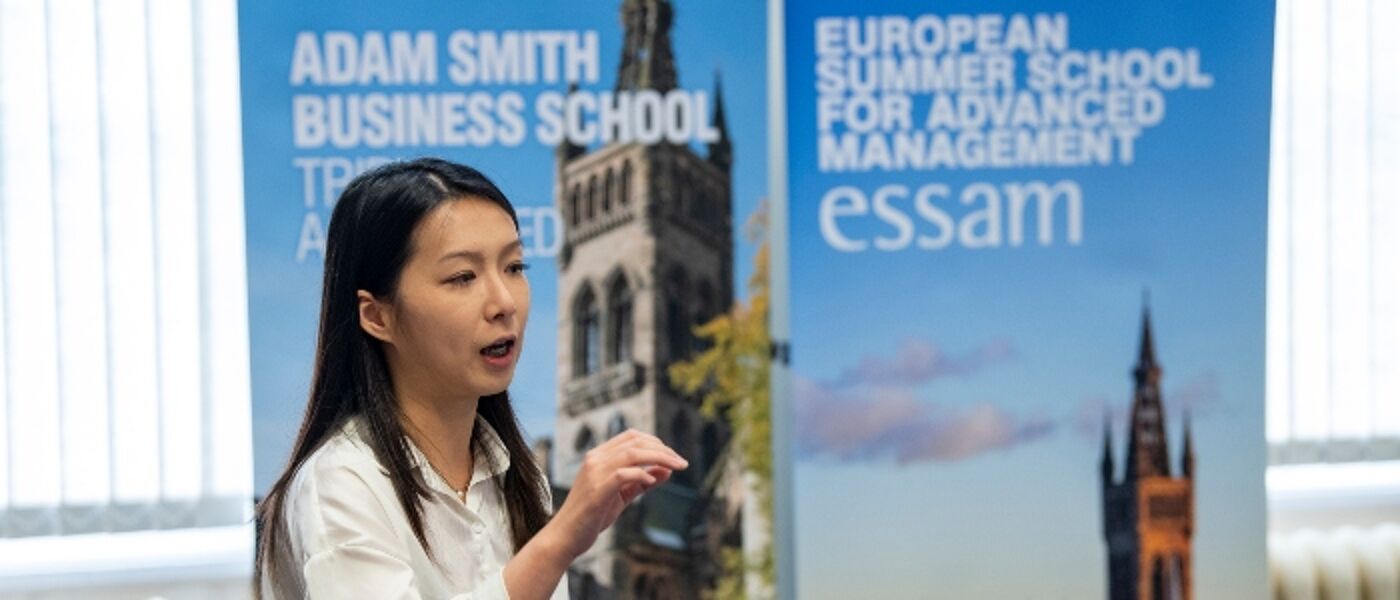Person presenting at ESSAM 2025 in front of an Adam Smith Business School banner stand