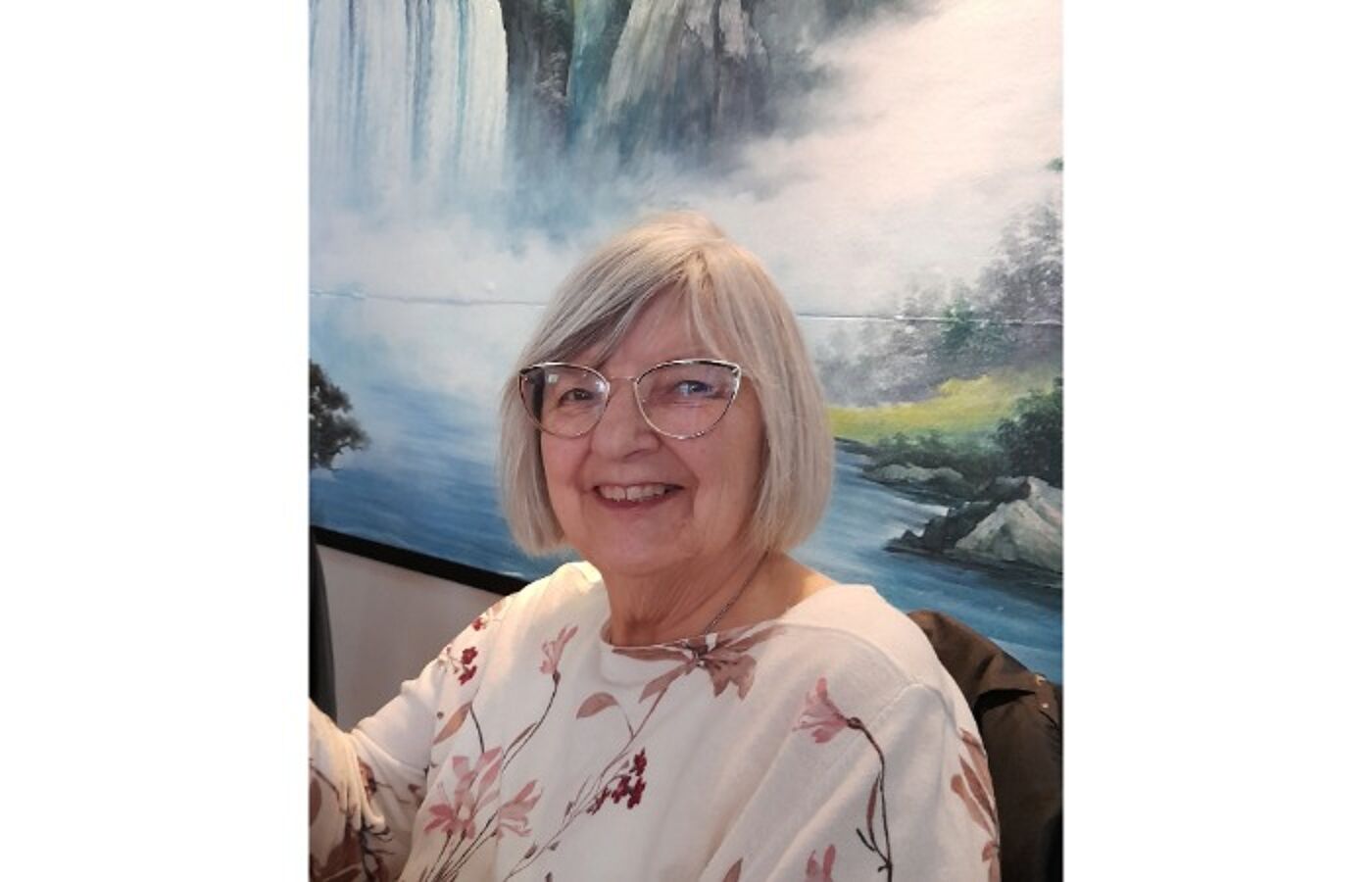 Sheena Wellington, sitting in front of a painting and smiling.