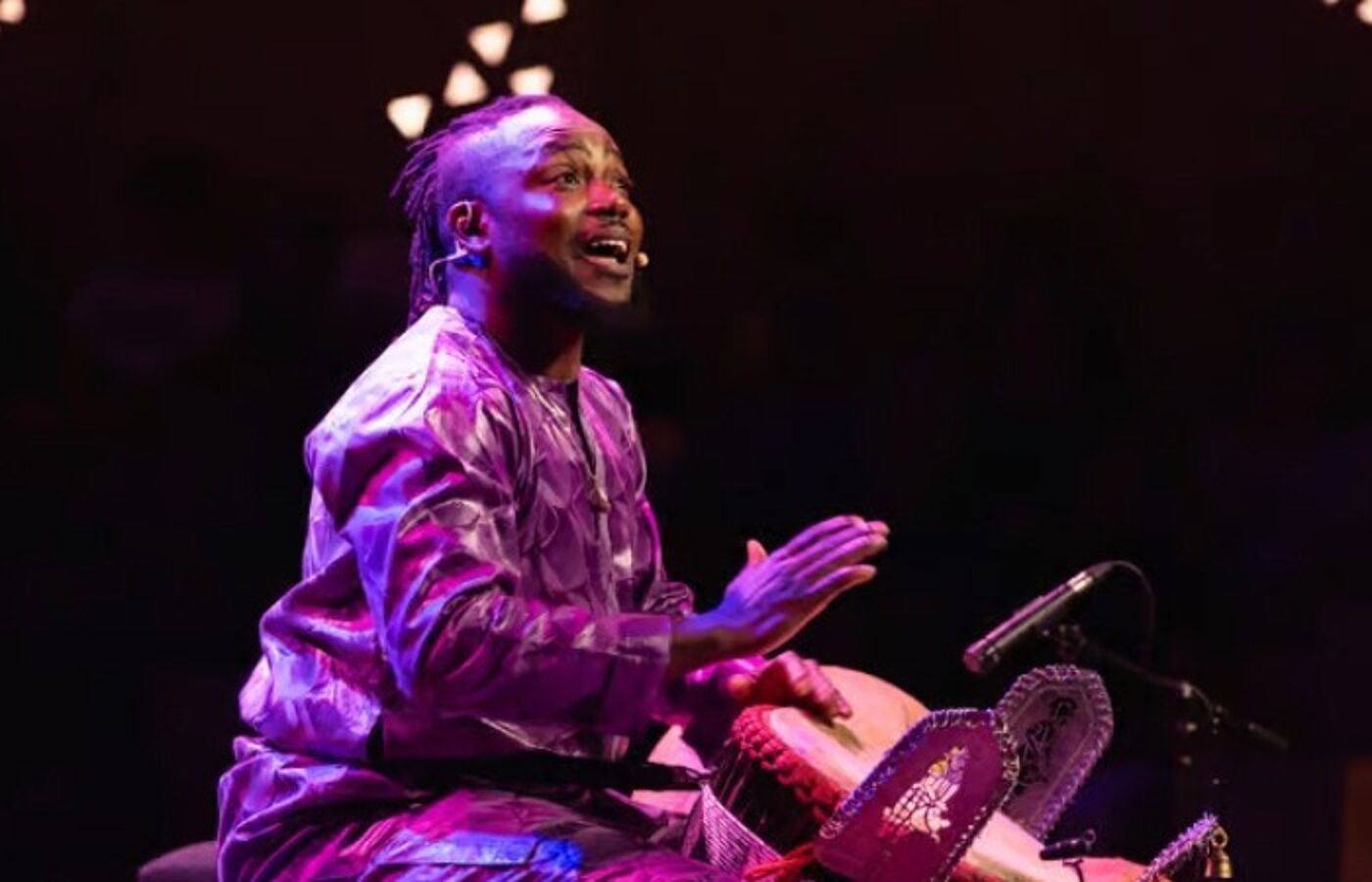Sidiki Dembele sits, playing a drum and singing
