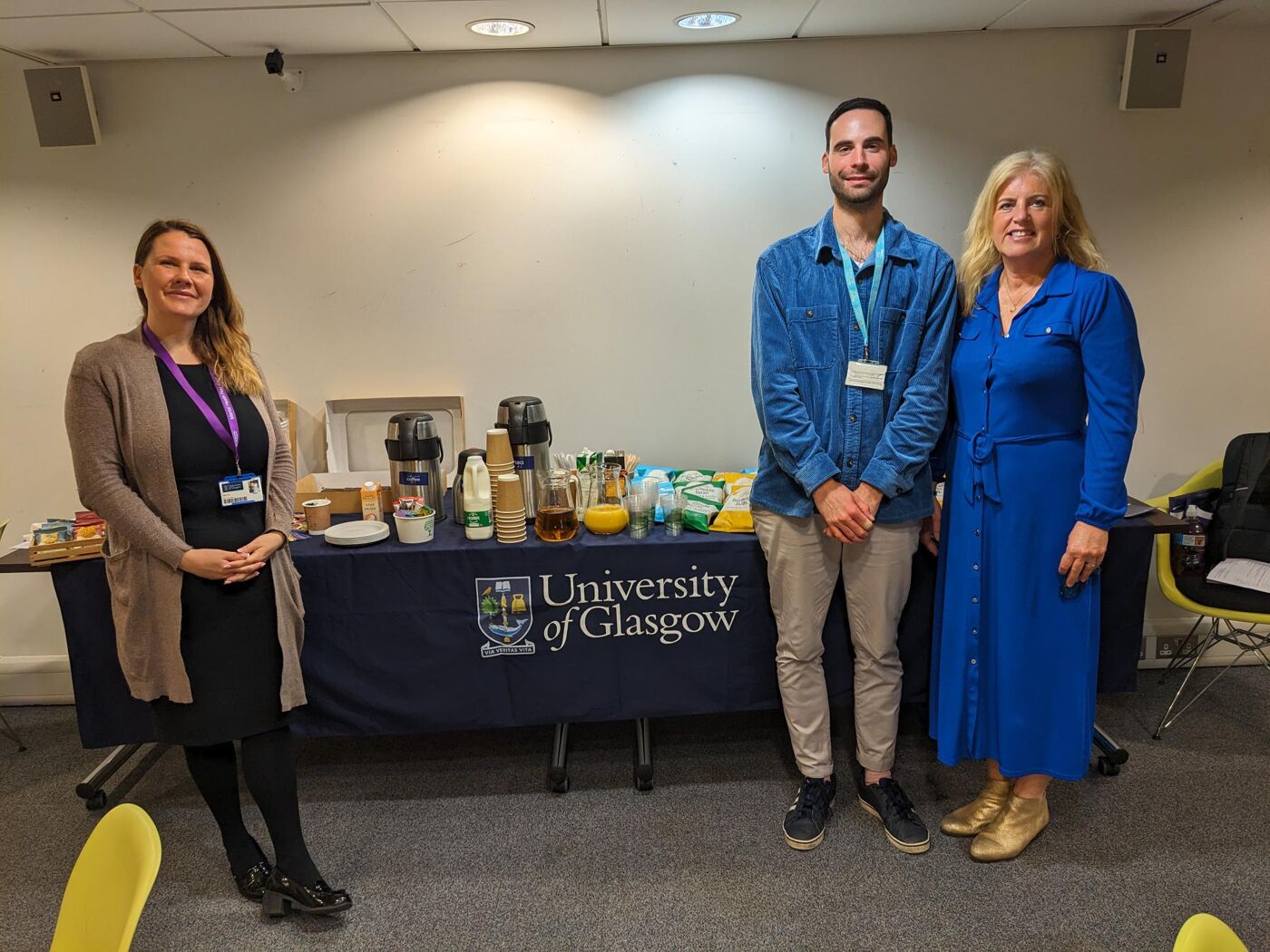 3 staff members stand in front of a table filled with tea, coffee and crisps