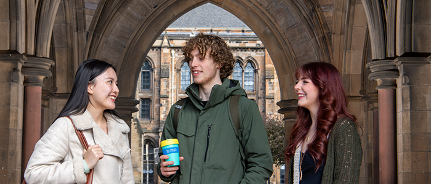 three students talking under at the west entrance of the Gilbert Scott building