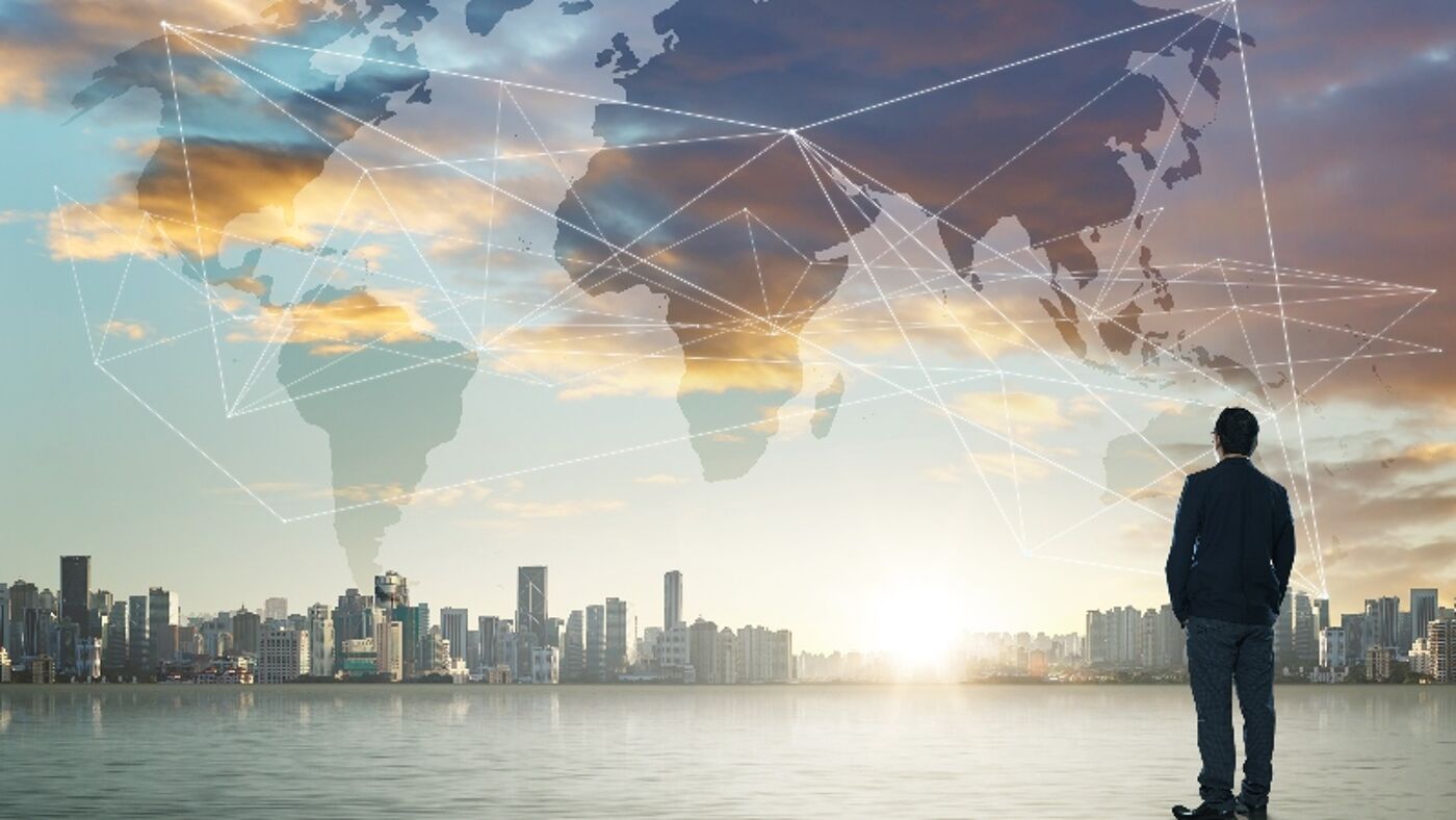 A picture of a man looking at a city skyline and a shadow of a international map full of connections