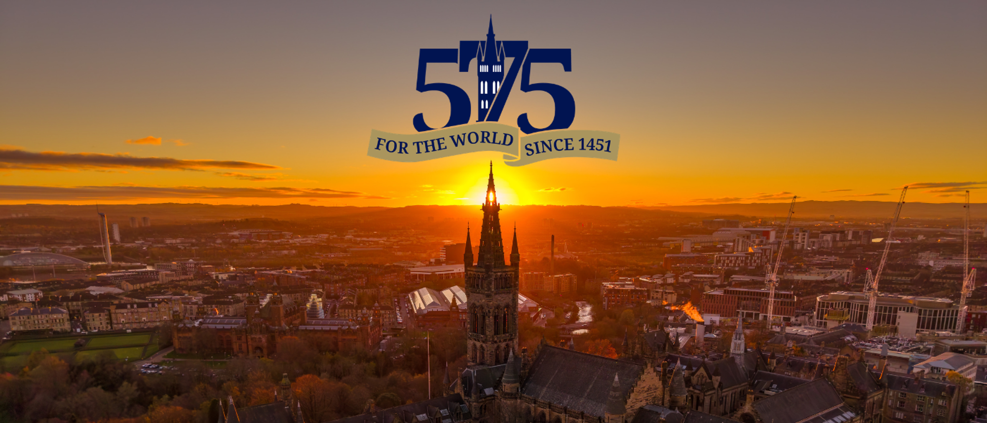A drone photo of the gilbert scott tower silhouetted against the sunset. The UofG 575 logo is above the tower