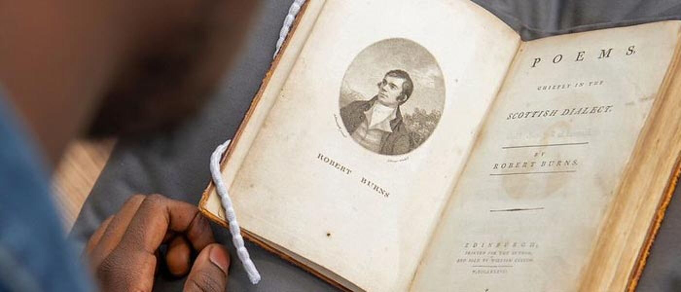 Photograph shot over the shoulder of a student showing them reading a collection of Robert Burns poems from the University's Special Collections.