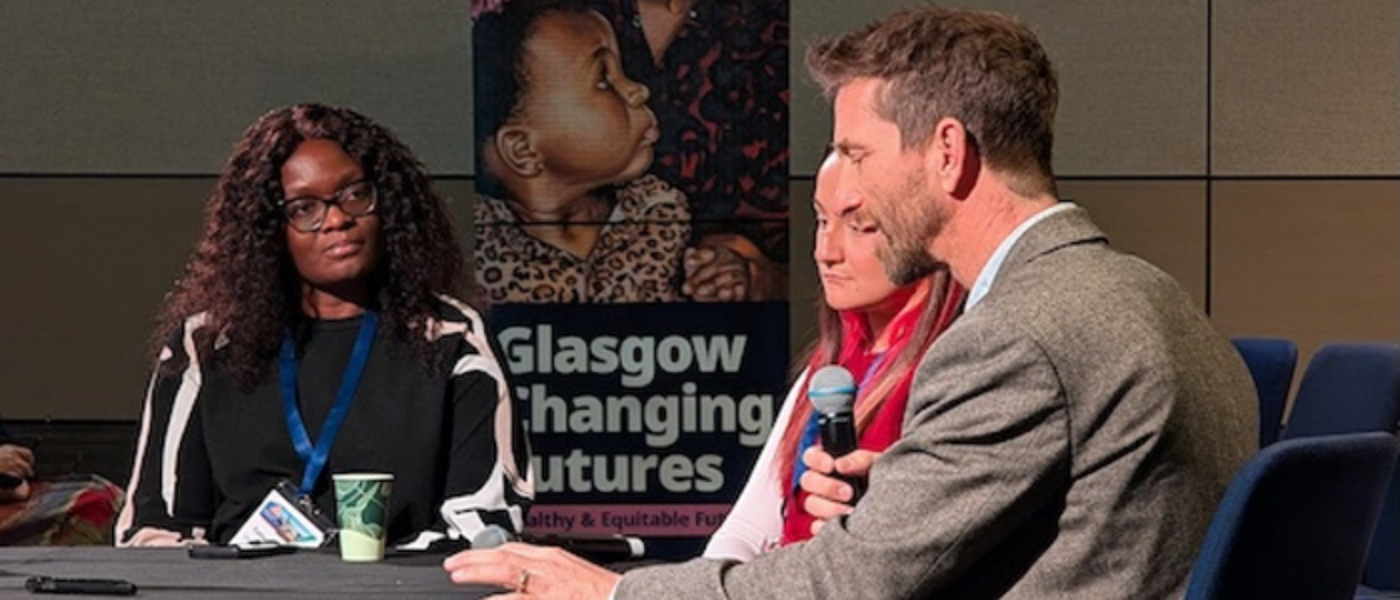 Three people around the table, one - a male - is holding a microphone and speaking