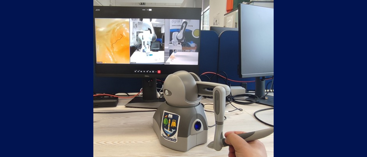 haptic controller manipulated by human hand connected to a robot arm which shows on the screen
