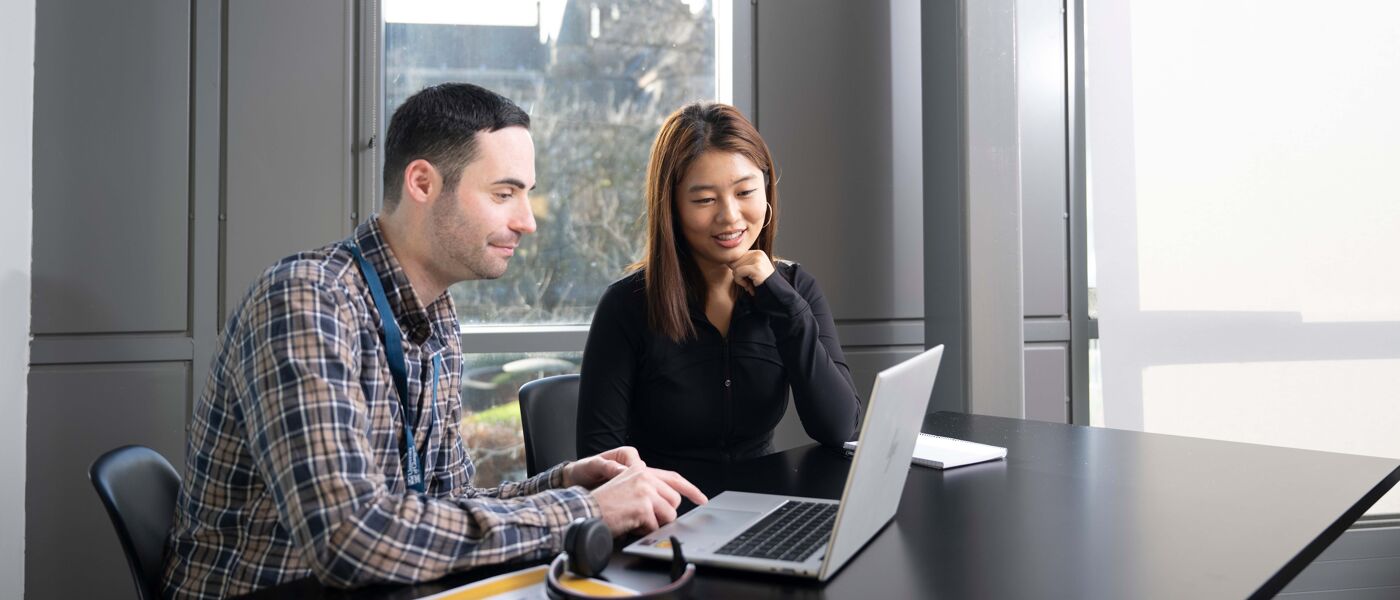 Two people sitting down and working together on a laptop
