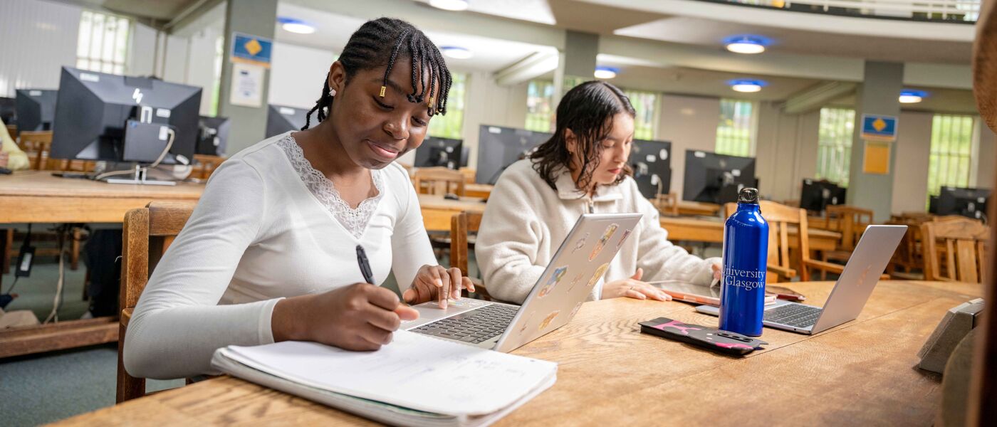 Two people sitting side by side at a table and working on laptops.