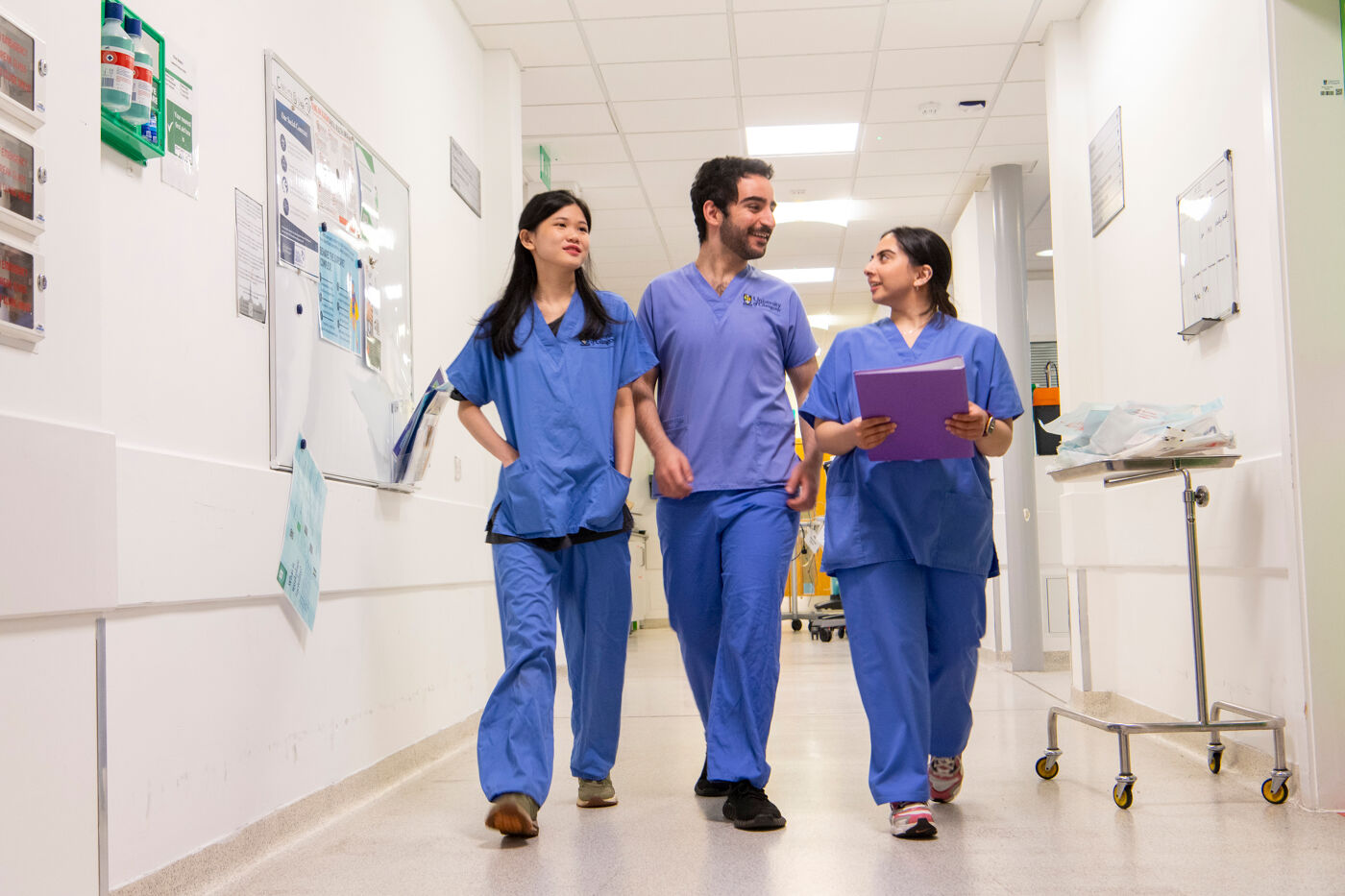 Three students in scrubs walking down a clinical corridor.