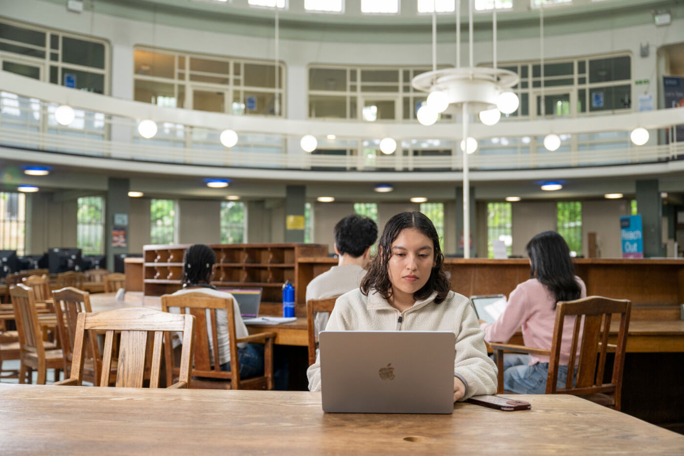 A student sits on their laptop at a desk in the circular reading room.
