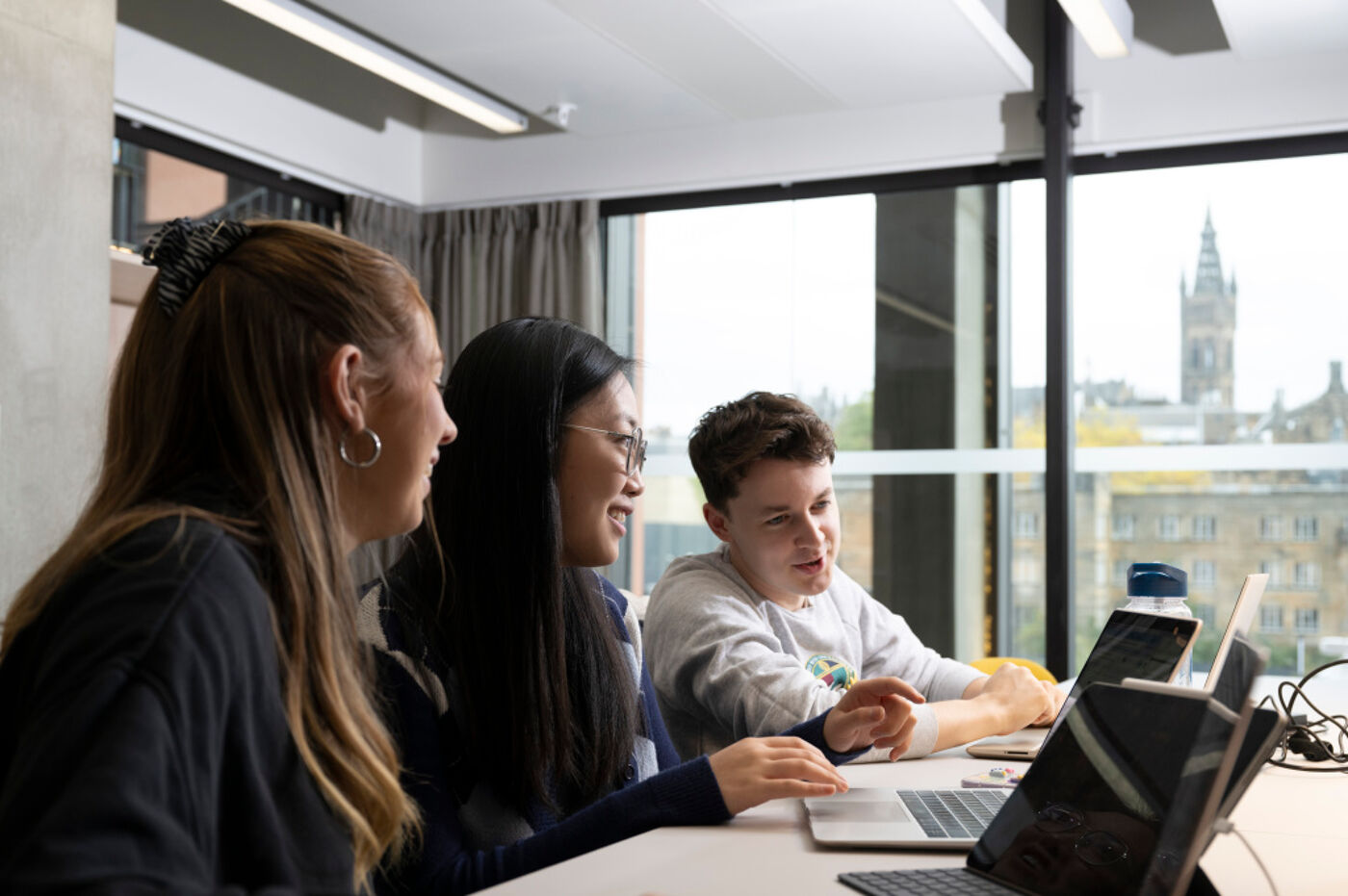 Three students sitting at a desk with their laptops.