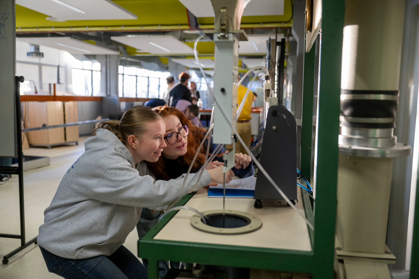 Two students looking closely at a complex looking set-up in an engineering lab.