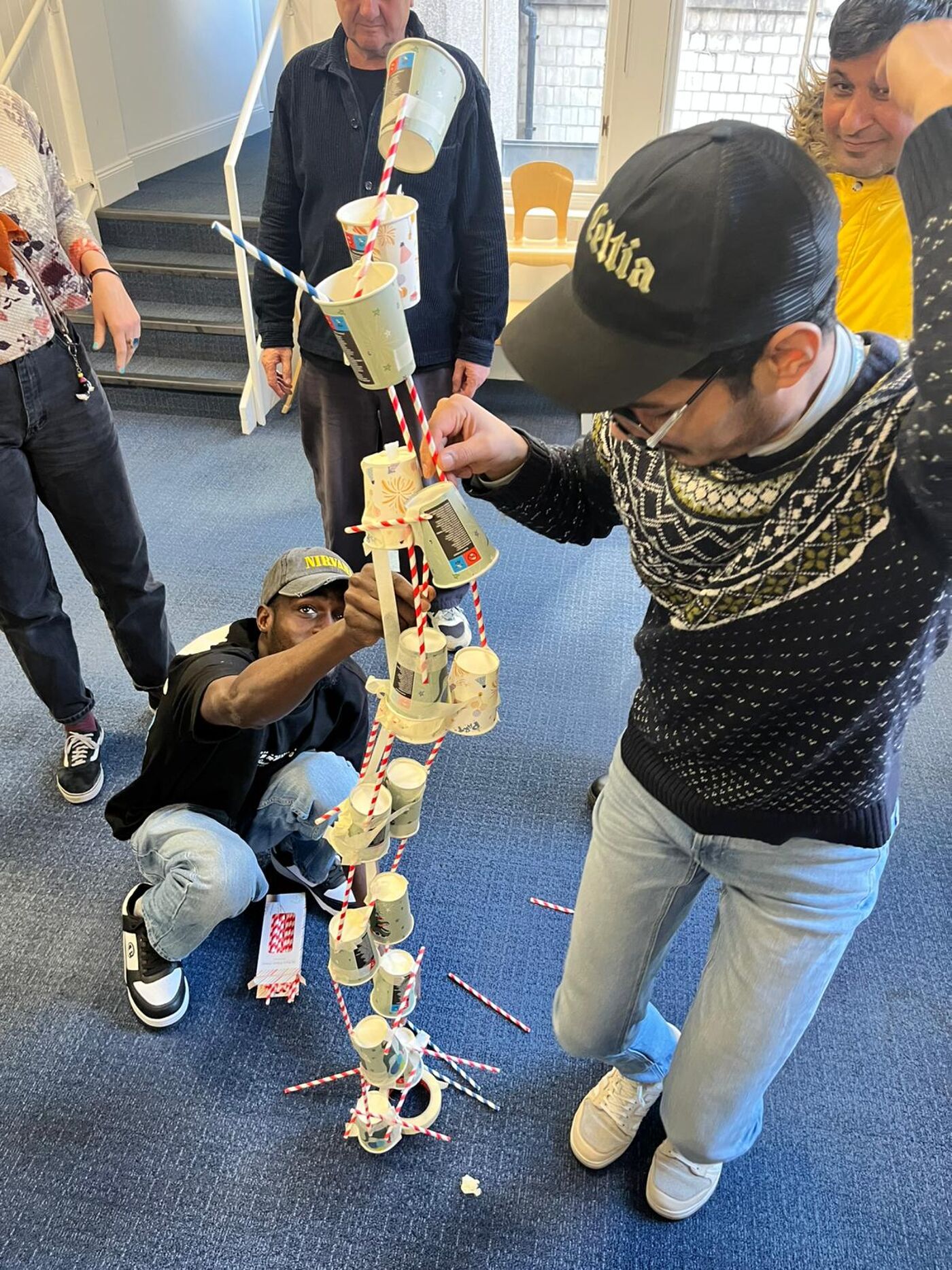 People work together to build a tall structure from paper cups, straws and tape during a creative workshop.